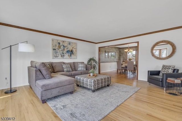 living room featuring baseboards, ornamental molding, light wood-style flooring, and a notable chandelier