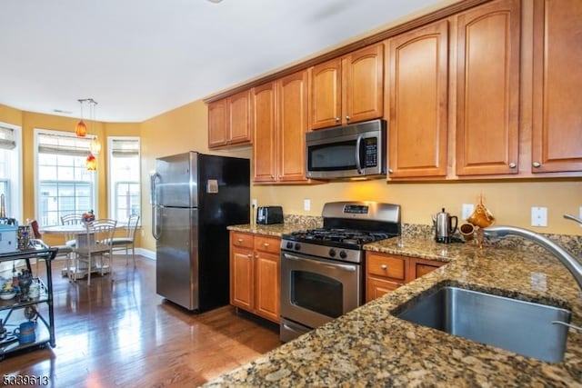 kitchen featuring stone counters, a sink, hanging light fixtures, appliances with stainless steel finishes, and brown cabinetry