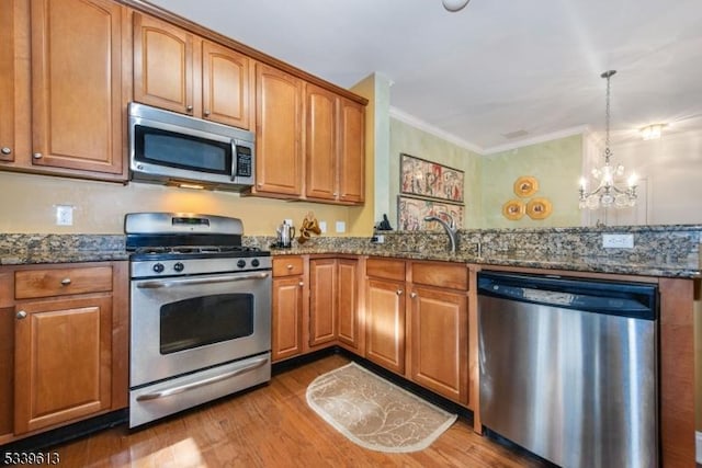 kitchen with pendant lighting, appliances with stainless steel finishes, dark stone countertops, and brown cabinets