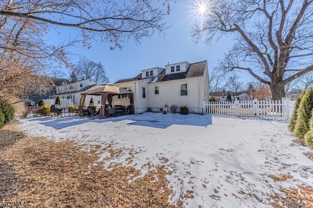 snow covered rear of property featuring a gazebo, fence, and a residential view