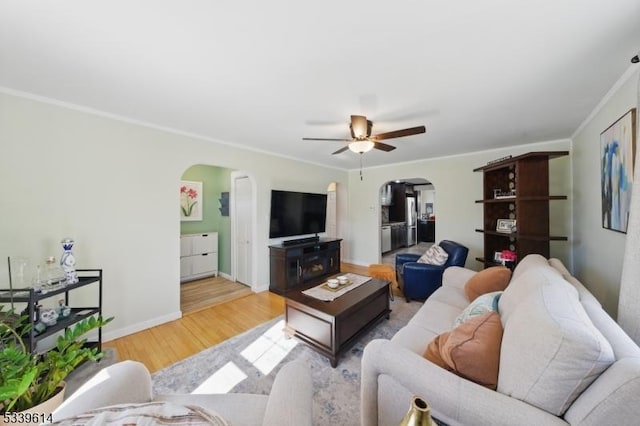 living area featuring arched walkways, baseboards, a ceiling fan, wood finished floors, and crown molding