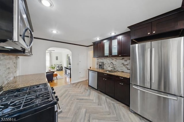 kitchen featuring arched walkways, appliances with stainless steel finishes, glass insert cabinets, a sink, and light stone countertops