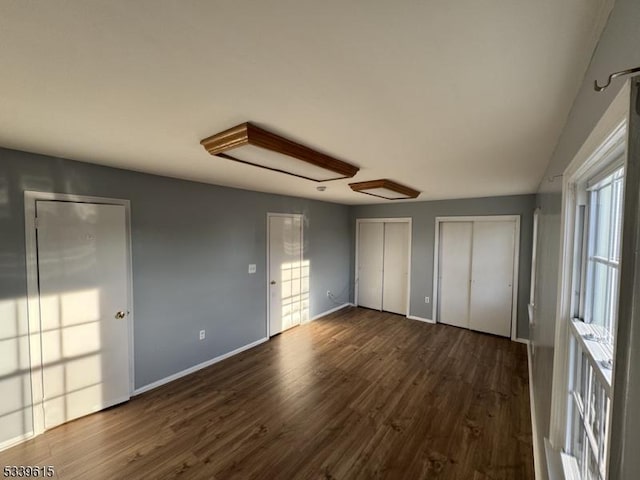 unfurnished bedroom featuring multiple closets, baseboards, and dark wood-style floors