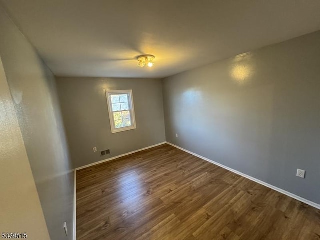 unfurnished room with dark wood-style floors, baseboards, and visible vents