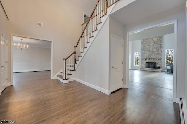 entryway with stairs, a stone fireplace, dark wood-type flooring, and visible vents