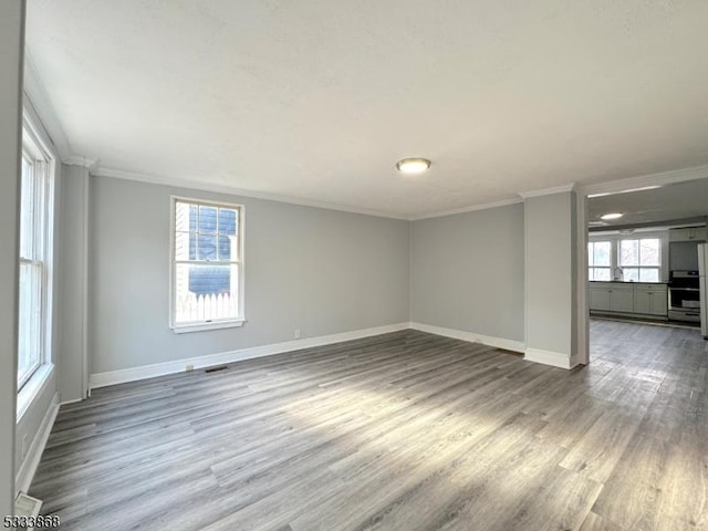 empty room featuring visible vents, crown molding, baseboards, and wood finished floors