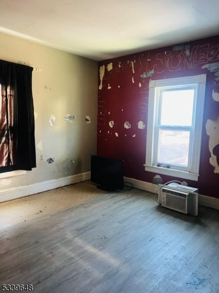 unfurnished room featuring baseboards, wood finished floors, and a wall mounted air conditioner