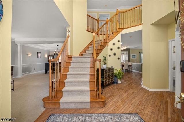 staircase with a notable chandelier, a high ceiling, wood finished floors, baseboards, and ornamental molding