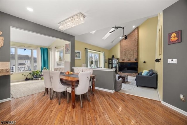 dining space featuring lofted ceiling with skylight, light wood-type flooring, and baseboards