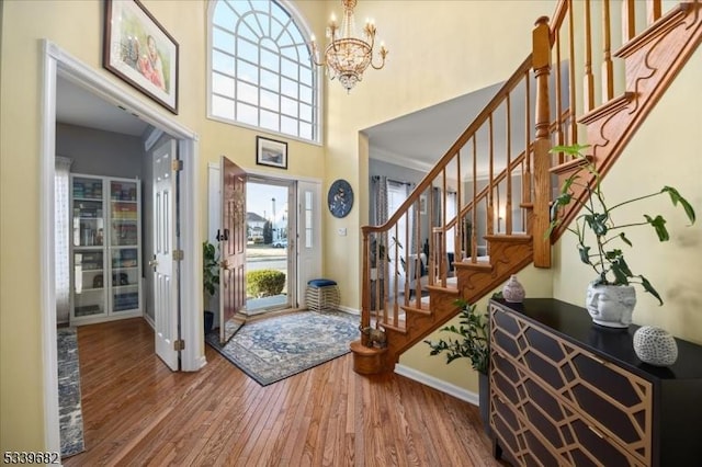 foyer with a chandelier, a high ceiling, wood finished floors, baseboards, and stairway