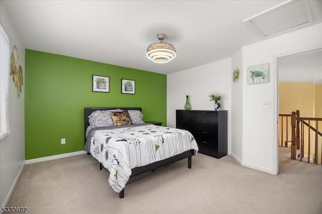 carpeted bedroom with an accent wall, attic access, and baseboards