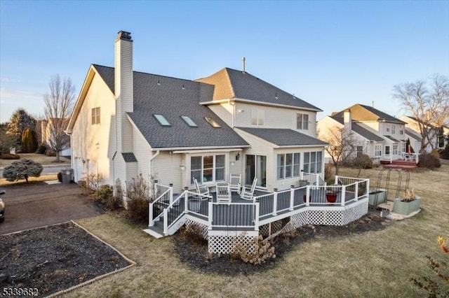 rear view of property with a yard, a wooden deck, a chimney, and roof with shingles