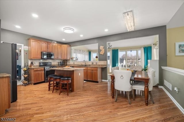 kitchen with a breakfast bar, a center island, stainless steel appliances, light wood-type flooring, and a sink