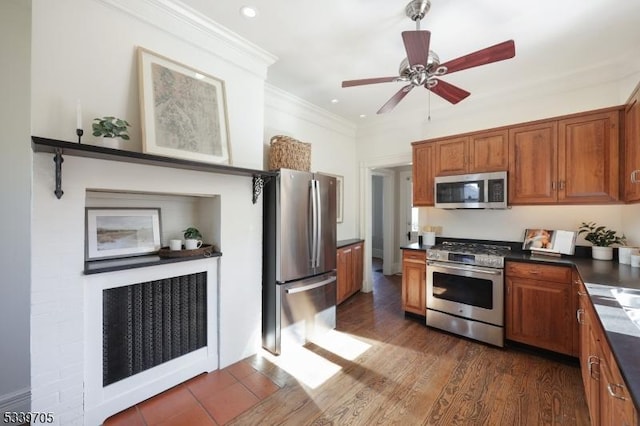 kitchen with dark wood-style flooring, brown cabinets, dark countertops, appliances with stainless steel finishes, and ornamental molding