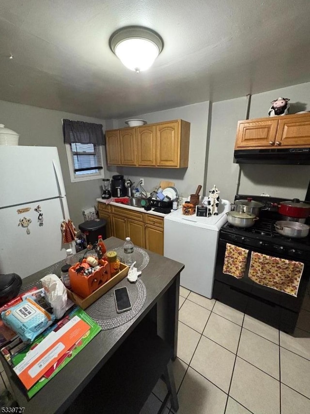 kitchen featuring black range oven, light tile patterned floors, washer / clothes dryer, freestanding refrigerator, and under cabinet range hood