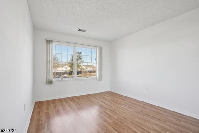 empty room with a textured ceiling, baseboards, visible vents, and light wood-style floors