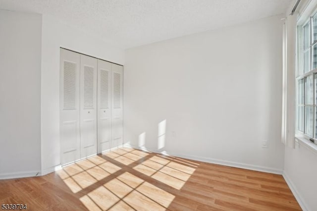 unfurnished bedroom featuring a closet, a textured ceiling, baseboards, and wood finished floors