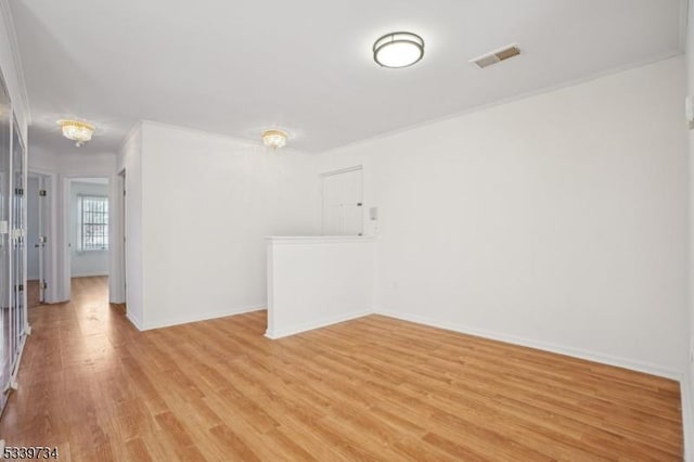 empty room featuring light wood-type flooring, baseboards, visible vents, and ornamental molding