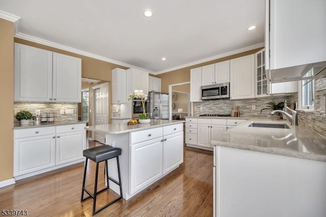 kitchen with appliances with stainless steel finishes, a center island, crown molding, white cabinetry, and a sink