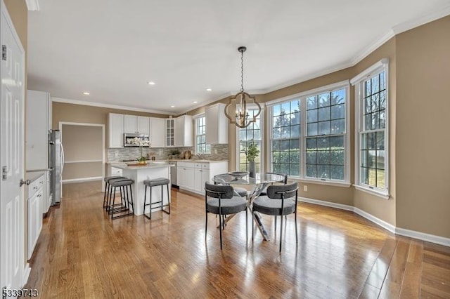 dining space featuring a chandelier, ornamental molding, wood finished floors, and baseboards