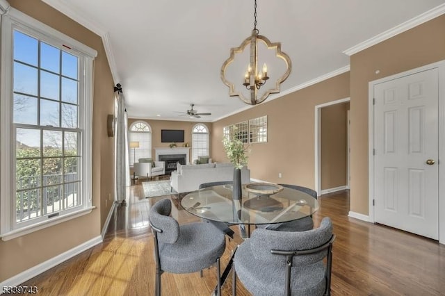 dining space with baseboards, a fireplace, ornamental molding, and wood finished floors