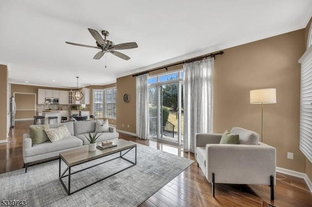 living area with a ceiling fan, crown molding, baseboards, and wood finished floors