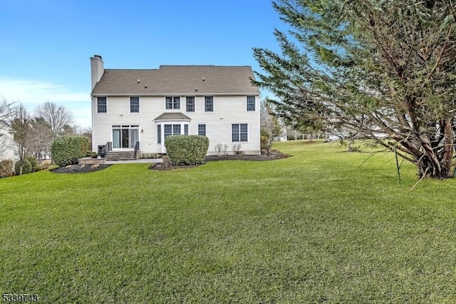 rear view of house featuring entry steps, a yard, and a chimney