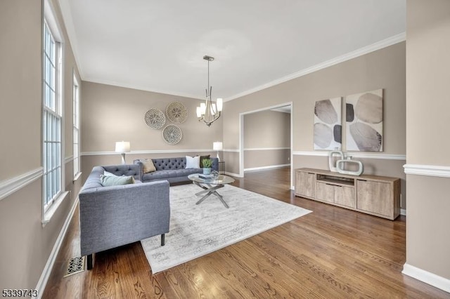 living area featuring crown molding, a notable chandelier, visible vents, wood finished floors, and baseboards