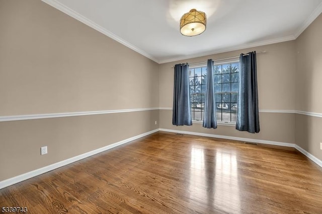 spare room featuring ornamental molding, visible vents, baseboards, and wood finished floors