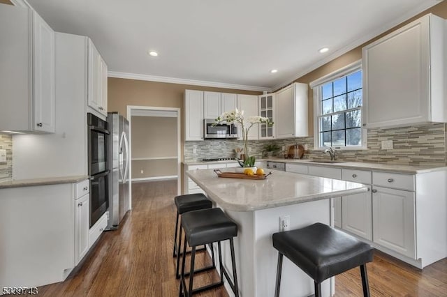 kitchen with stainless steel appliances, white cabinetry, a sink, a kitchen island, and a kitchen bar