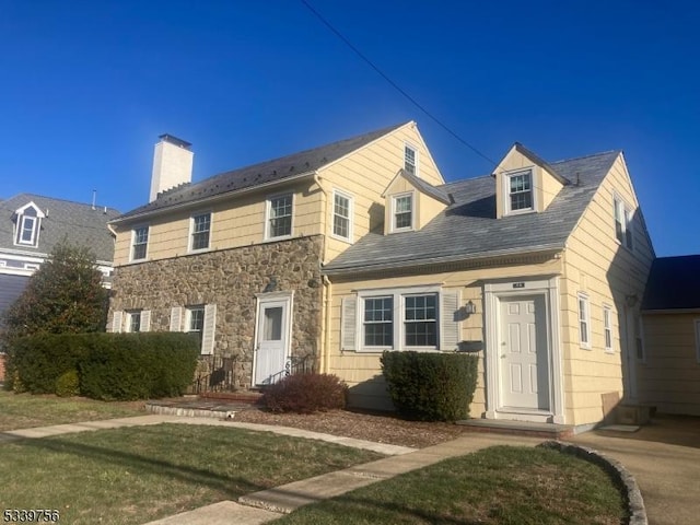 view of front of home featuring stone siding, a front lawn, and a chimney