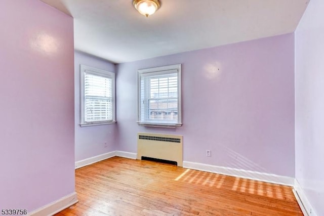 unfurnished room with radiator, light wood finished floors, and baseboards