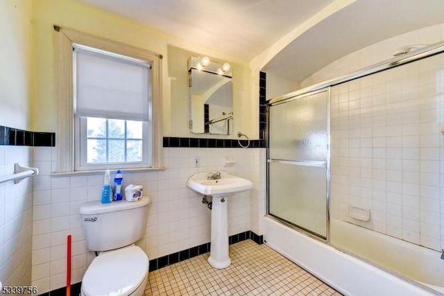 full bath with toilet, bath / shower combo with glass door, tile walls, wainscoting, and tile patterned floors