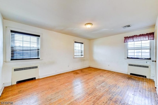 unfurnished room with radiator heating unit, visible vents, and wood-type flooring