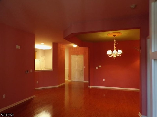 spare room with a chandelier, baseboards, and wood finished floors