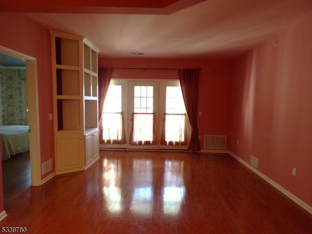 empty room with wood finished floors, visible vents, and baseboards