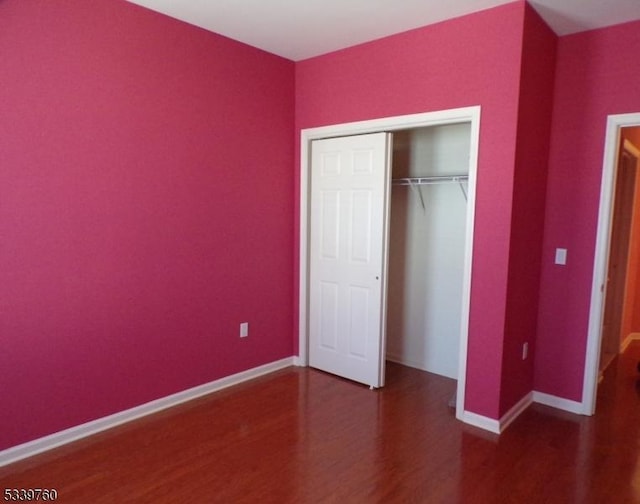 unfurnished bedroom featuring dark wood-style floors, a closet, and baseboards