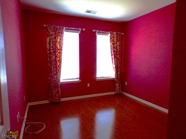 spare room with wood finished floors, visible vents, and baseboards