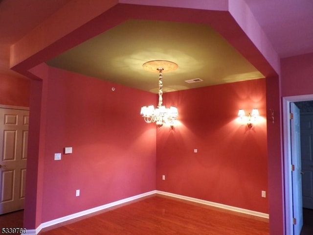 empty room with baseboards, visible vents, a chandelier, and wood finished floors