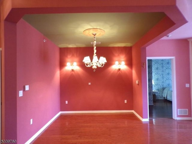 empty room featuring wood finished floors, visible vents, baseboards, and an inviting chandelier