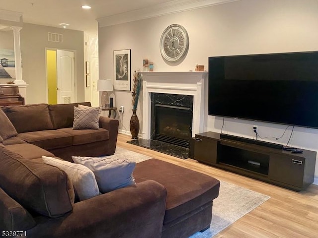 living area with decorative columns, light wood finished floors, recessed lighting, visible vents, and a premium fireplace