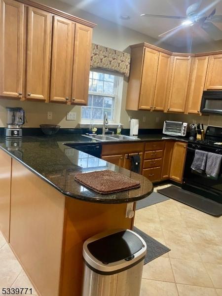 kitchen with a ceiling fan, a sink, black appliances, a peninsula, and a kitchen breakfast bar