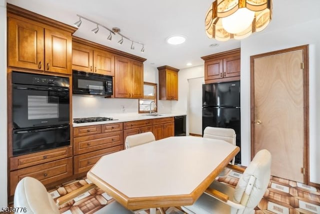 kitchen with a sink, light countertops, black appliances, brown cabinetry, and pendant lighting