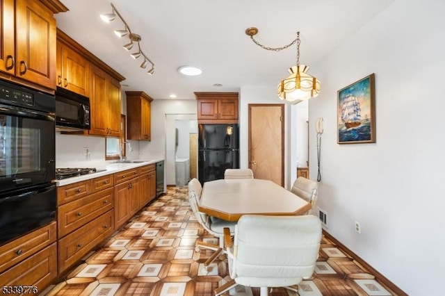 kitchen featuring light countertops, a warming drawer, black appliances, brown cabinetry, and pendant lighting