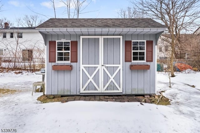 snow covered structure with an outbuilding, a storage unit, and fence