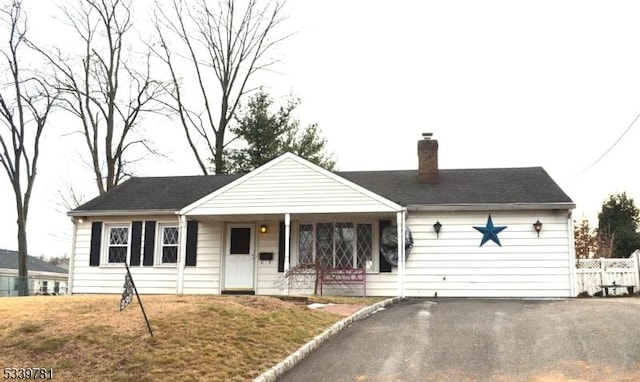 view of front of property featuring driveway, a chimney, a front lawn, and fence