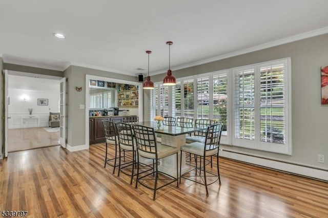 dining room featuring a baseboard heating unit, baseboards, ornamental molding, and light wood finished floors