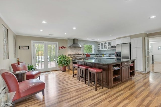 kitchen featuring stainless steel fridge, white cabinets, a center island, french doors, and wall chimney range hood