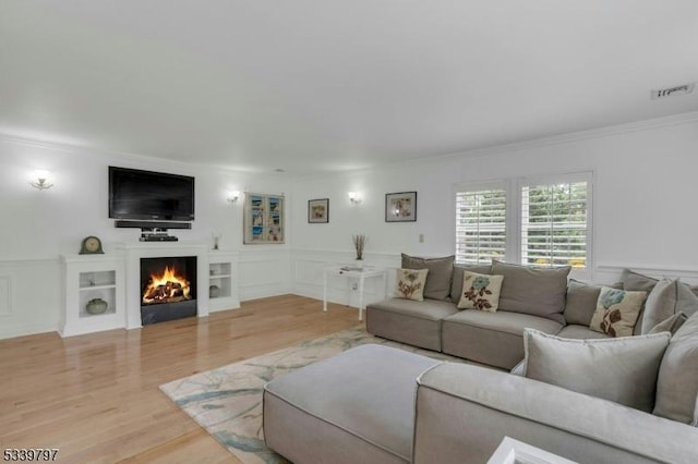 living area featuring visible vents, wood finished floors, a lit fireplace, crown molding, and a decorative wall