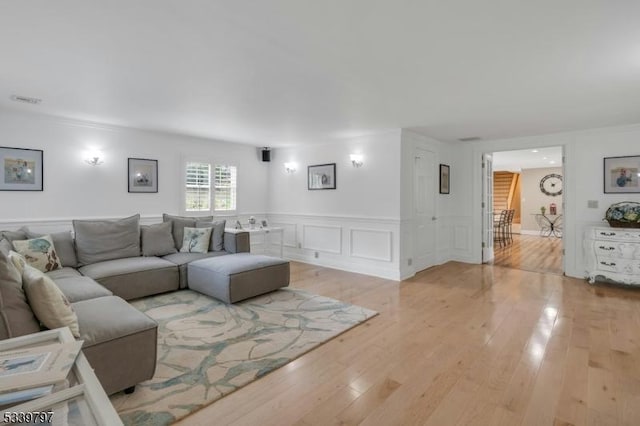 living room featuring a wainscoted wall, light wood-type flooring, visible vents, and a decorative wall